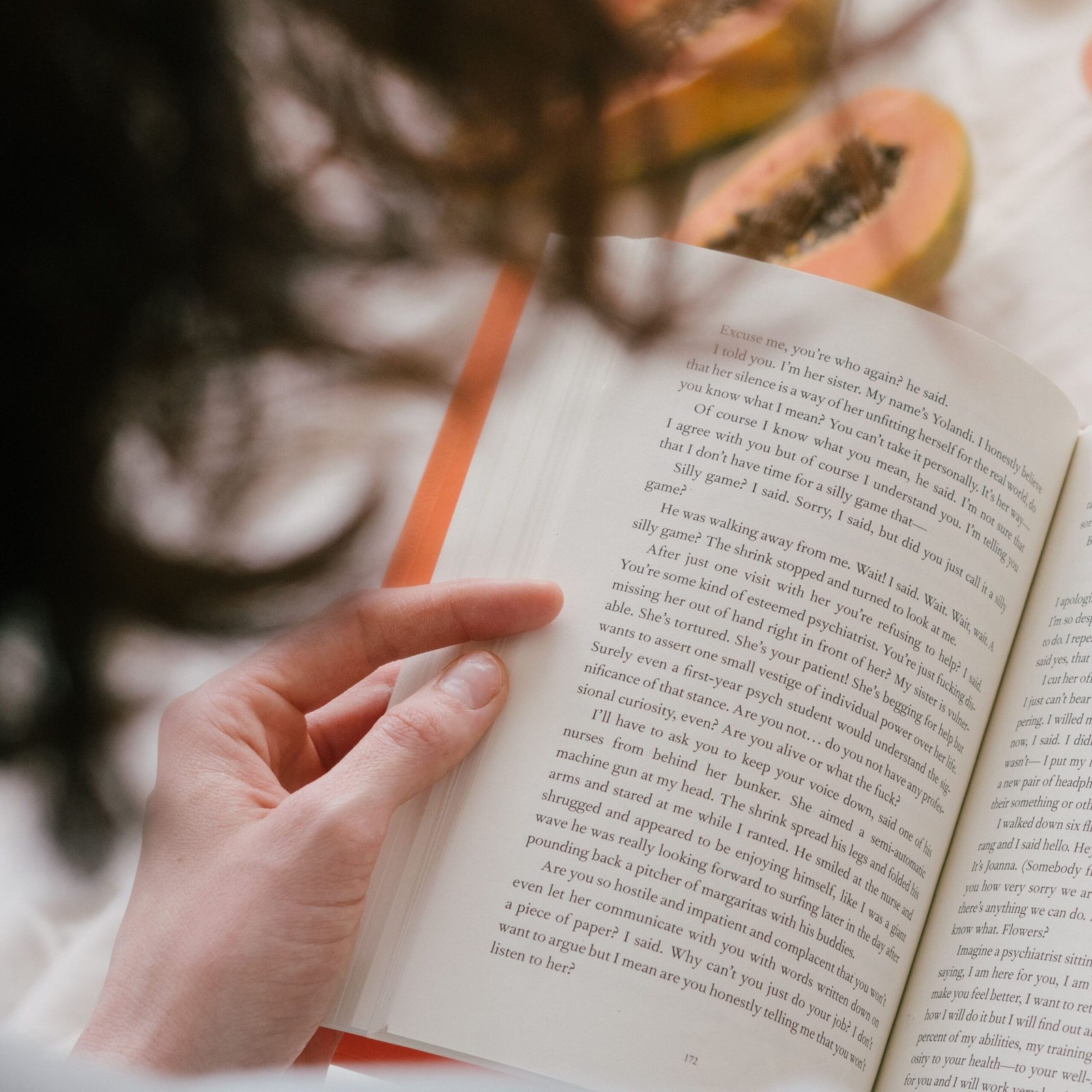 The Way Out A person enjoys reading a book surrounded by fresh papaya, grapes, and a drink, creating a cozy indoor scene.