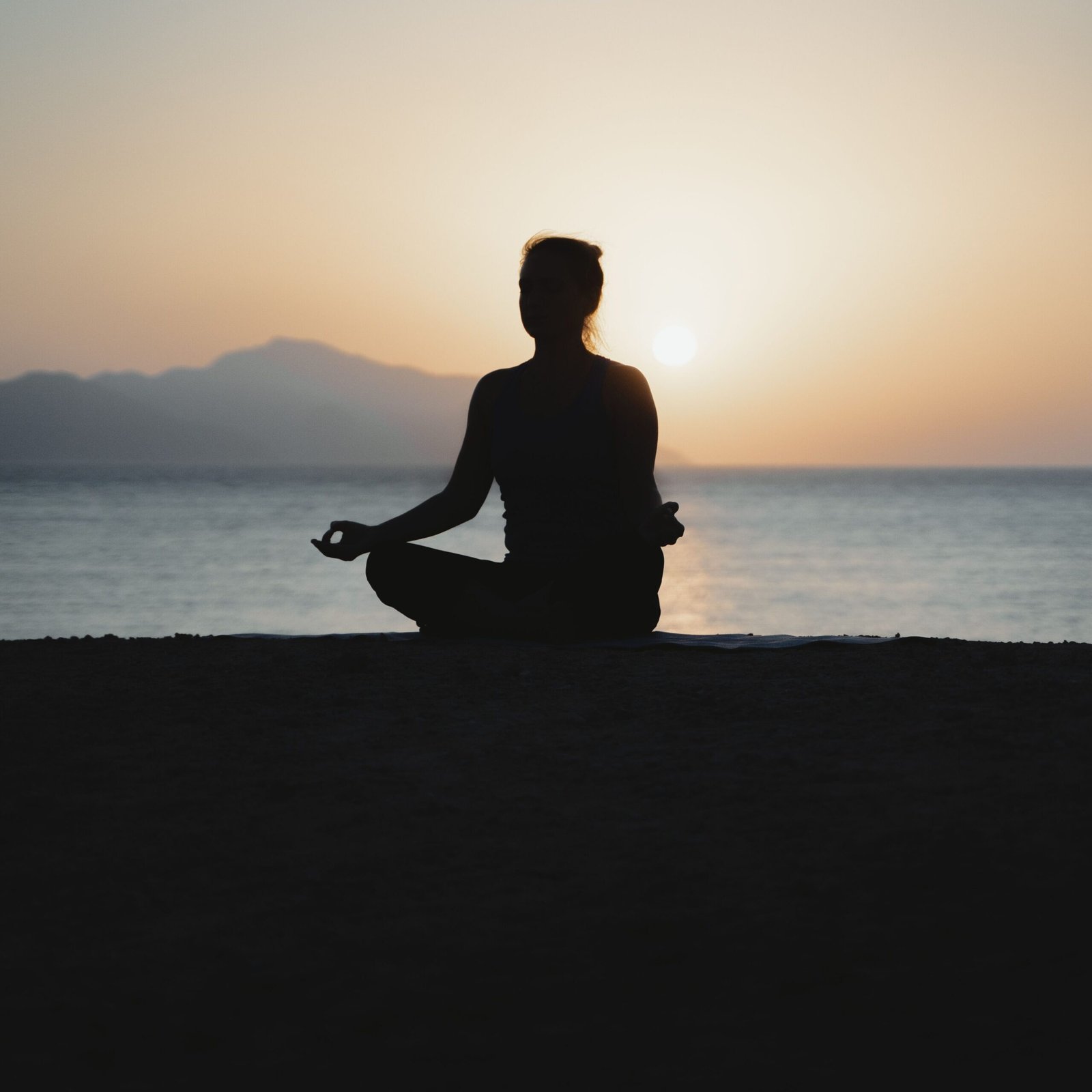 A woman practices meditation with a tranquil ocean sunset backdrop, embodying peace and relaxation.